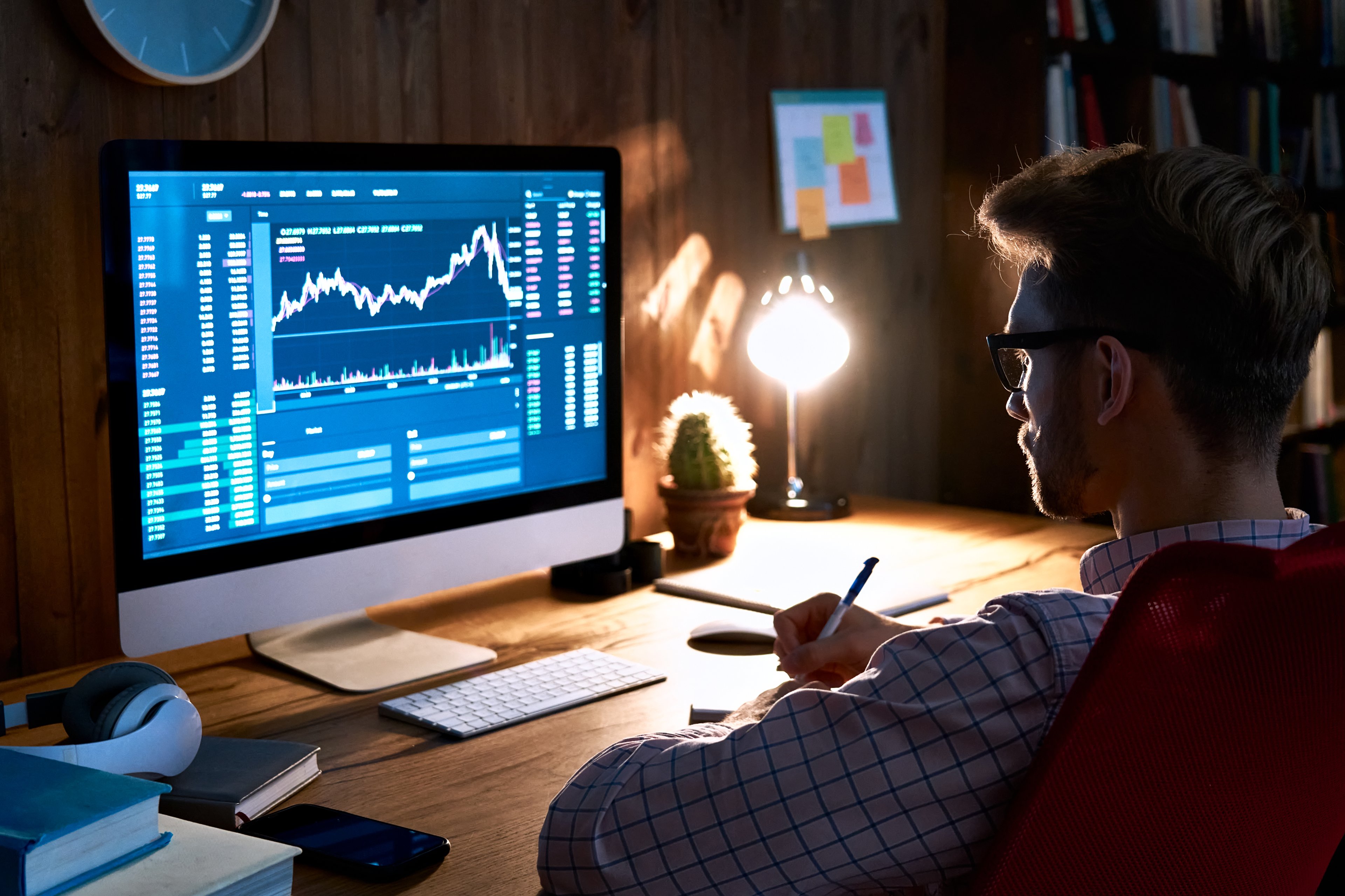 An investor sitting in a dark room looking at their computer screen, which is displaying a stock or cryptocurrency chart
