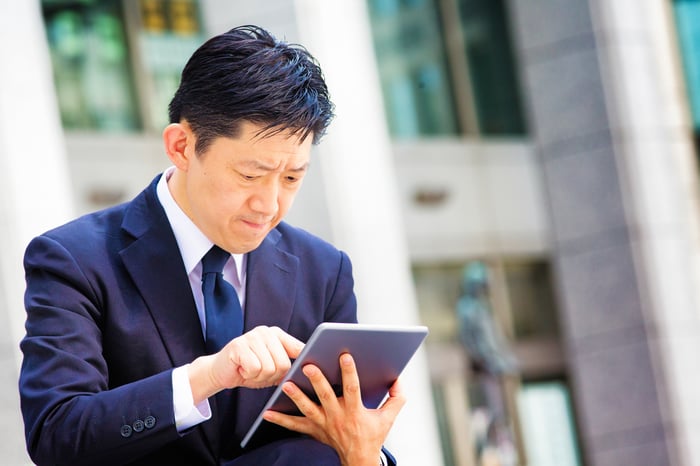 A person with a stressed expression is outside using a tablet.