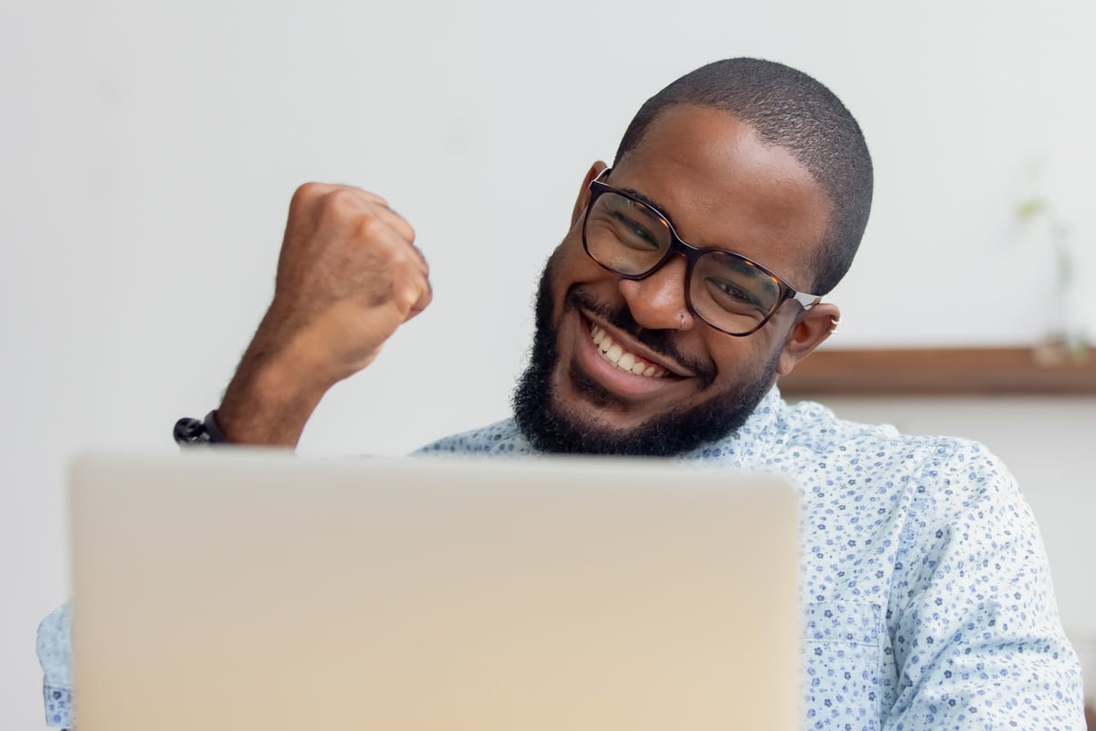 An investor clenches their fist and smiles in celebration as they look at a laptop.