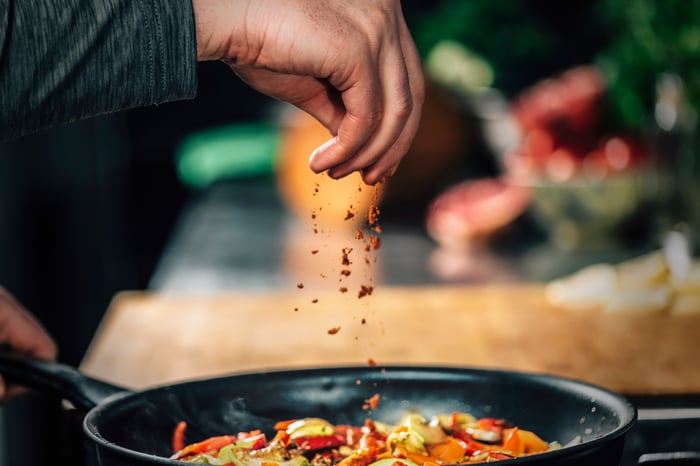 A hand adding spices to food. 