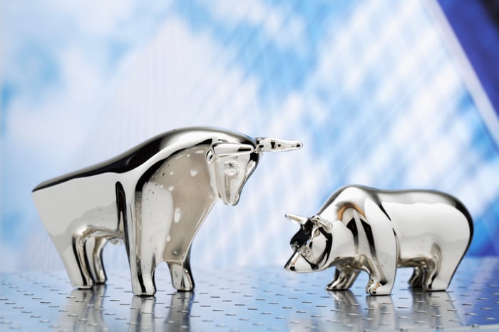 Silver bull and bear figurines on a blue backdrop.