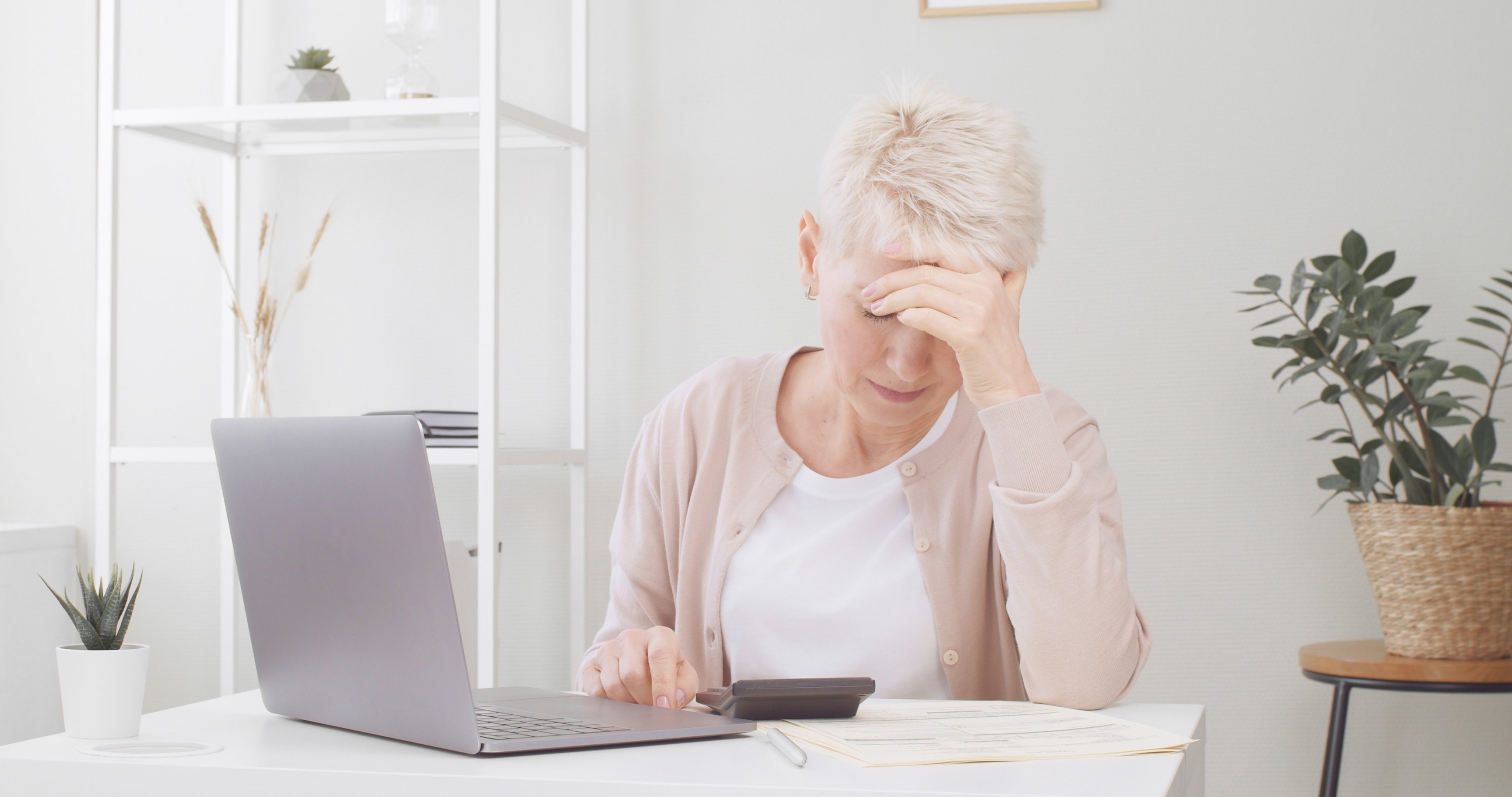 A person at a table with a laptop holding their head_GettyImages-1342983347
