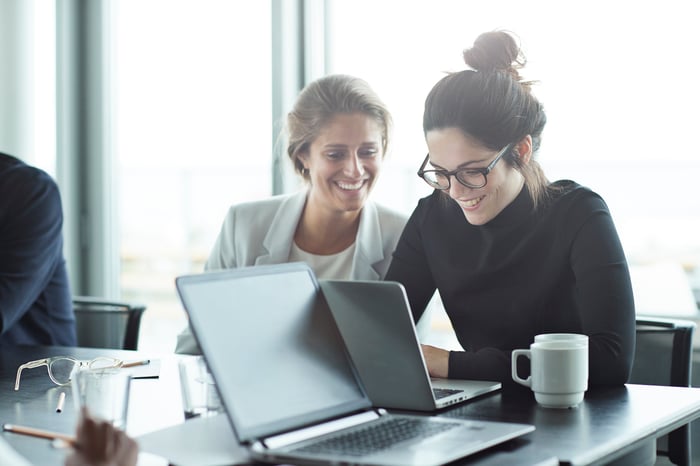 Professionals smiling while working together on a laptop in an office.