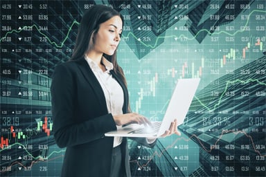 A person standing typing on a laptop with stock market quotes in the background