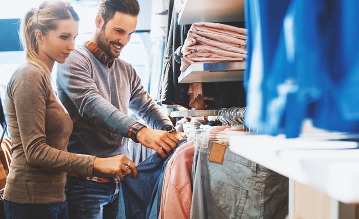People are smiling while shopping for jeans in a retail store. 