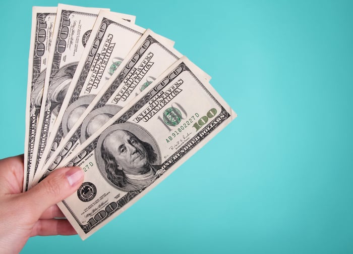 A hand is holding five fanned-out $100 bills.