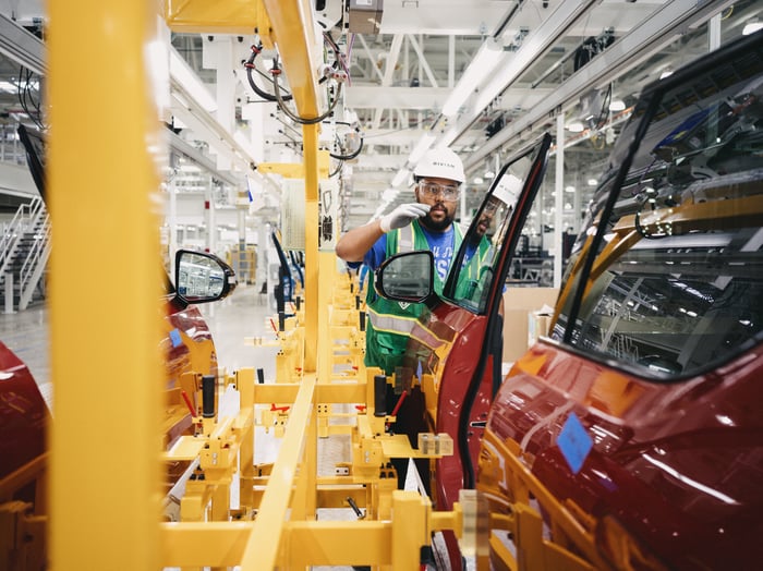 A auto manufacturing plant worker installs a door on a Rivian electric vehicle