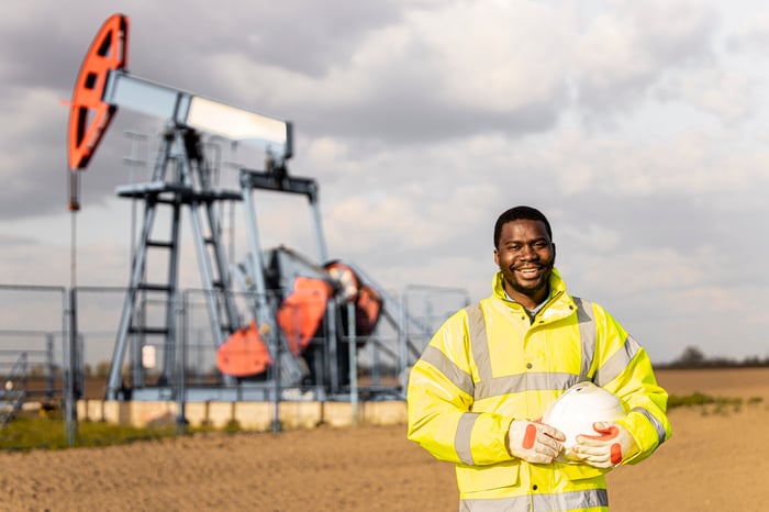 Oil derrick on land with smiling technician. 