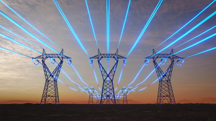 High-voltage transmission lines glowing blue against the backdrop of a setting sun.