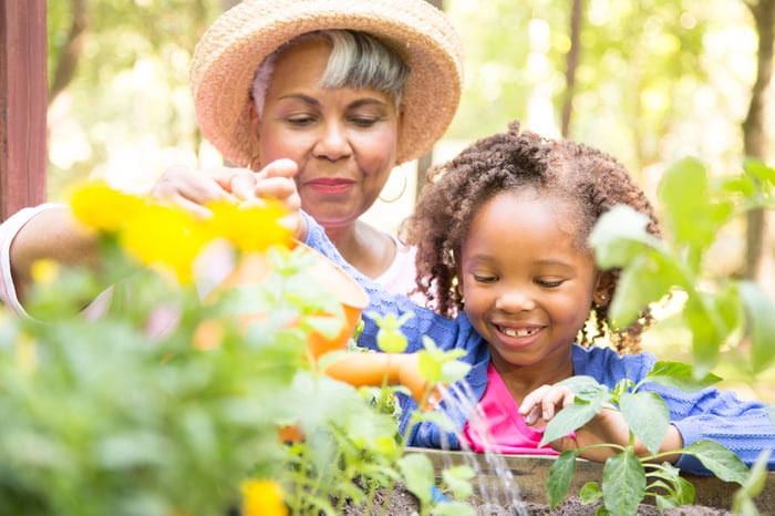 Senior and child watering plants together.