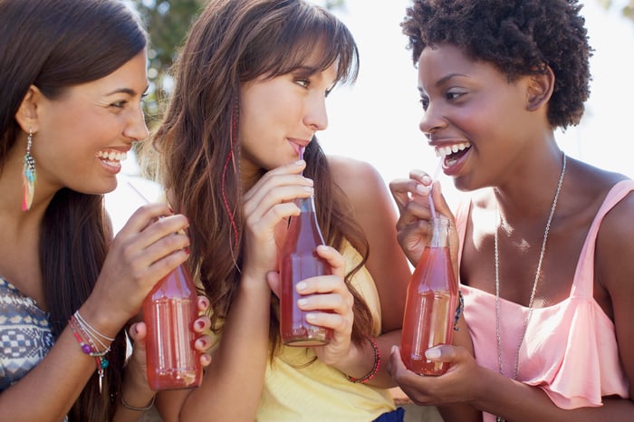 Three friends sip colorful beverages from soda bottles with straws.