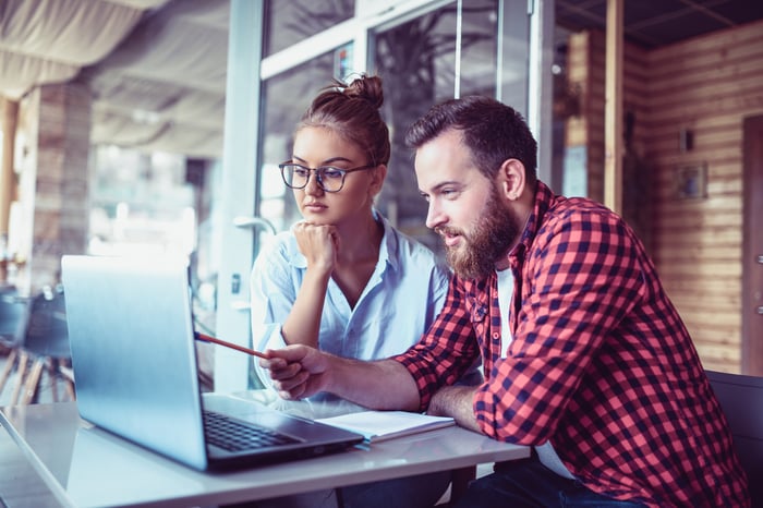 A young couple sitting together in a cafe and using a laptop to help them make investing decisions. 