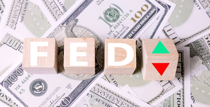 Fed letters with green and red arrow on top of hundred dollar bills.