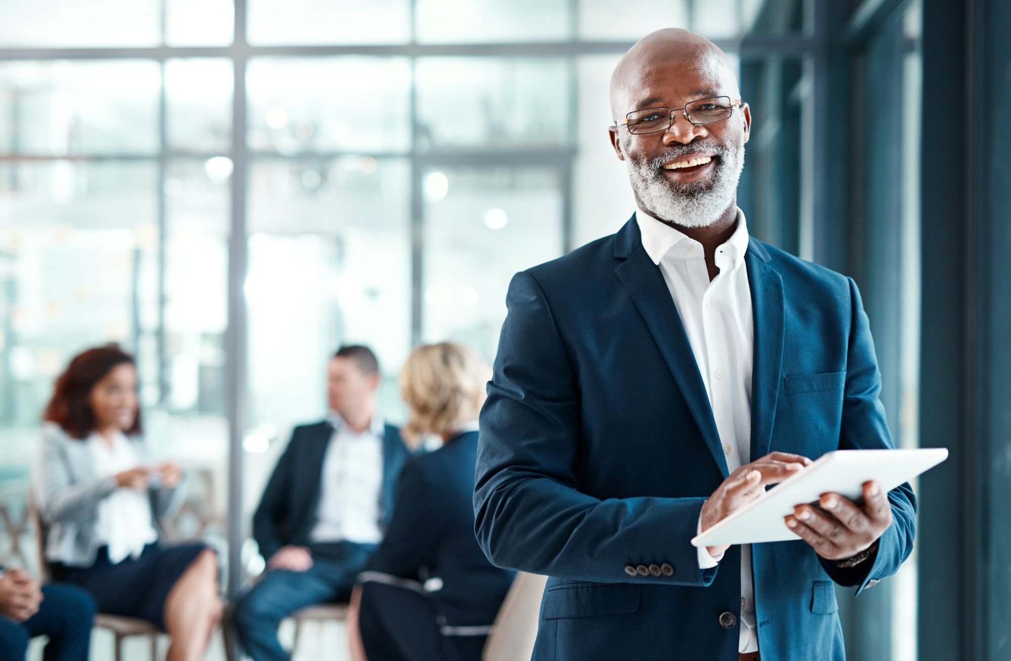 An executive holding a tablet in front of other employees.