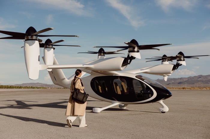 A passenger with a carry-on bag approaches a Joby Aviation eVTOL on the tarmac. 