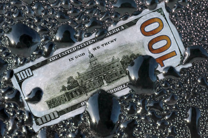 A $100 bill surrounded by drops of oil.