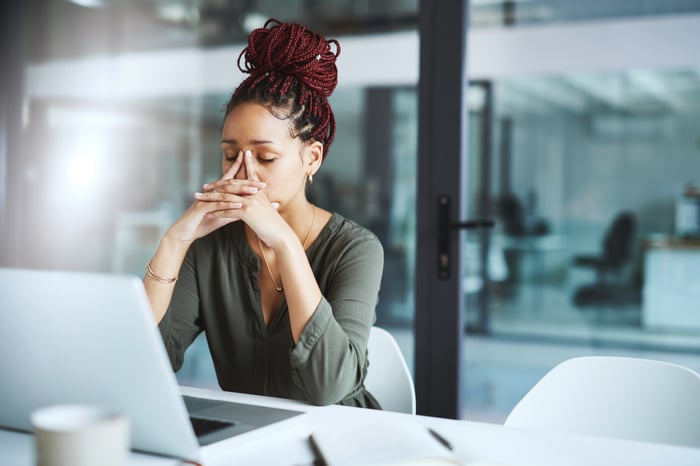 A person in a thoughtful pose, using a laptop in a modern office.