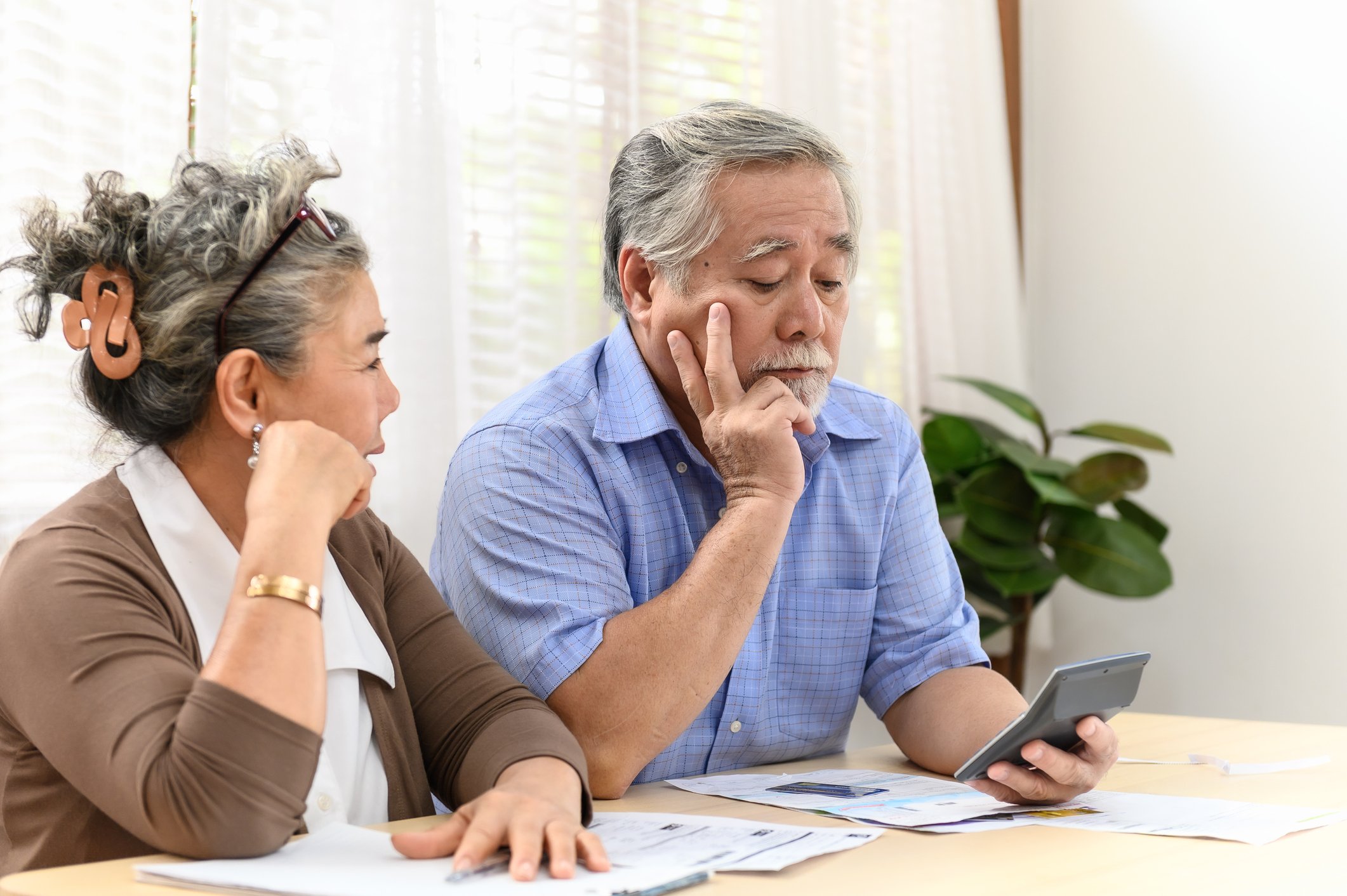 A visibly worried couple examining bills and financial statements laid out on a table in front of them.