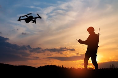 Soldier operating quadcopter drone against a sunset.
