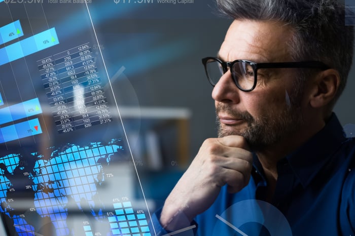 Person with a hand on their chin looking at numbers on a screen. 