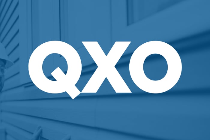 white QXO logo set over blue shaded view of a home under construction. 