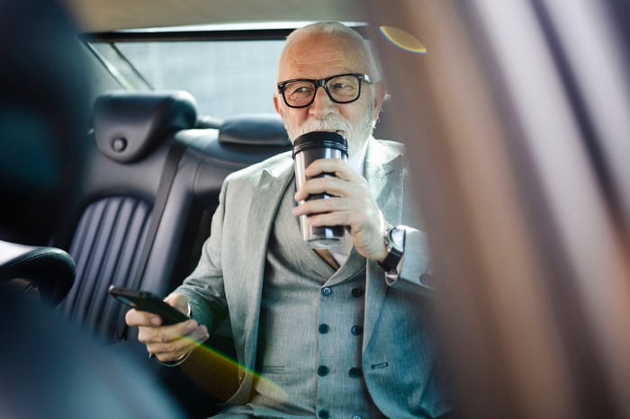 An older person in a car drinking.