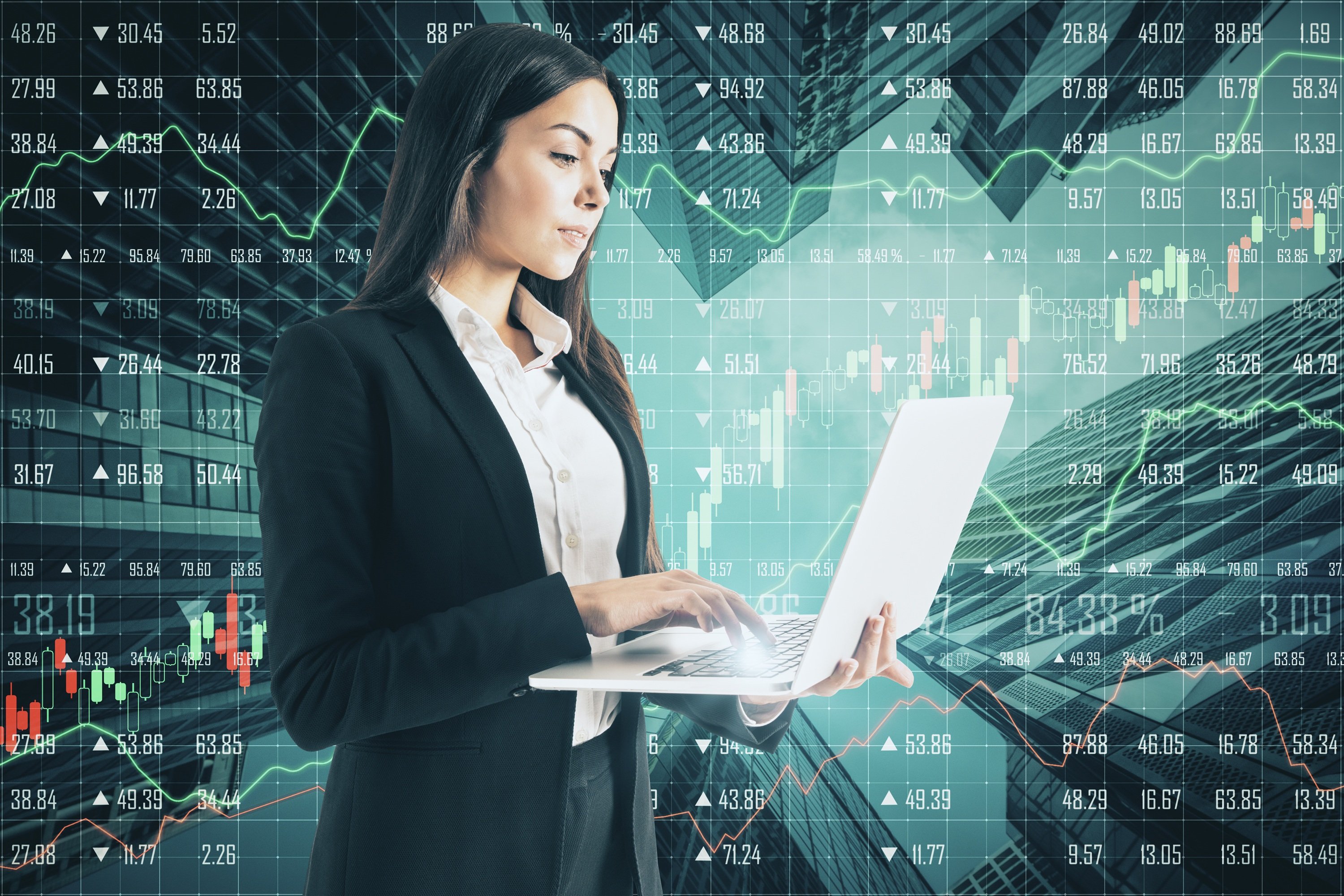 A person standing typing on a laptop with stock market quotes in the background