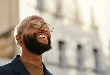 A person smiles while standing outside, with a blurred building in the background.