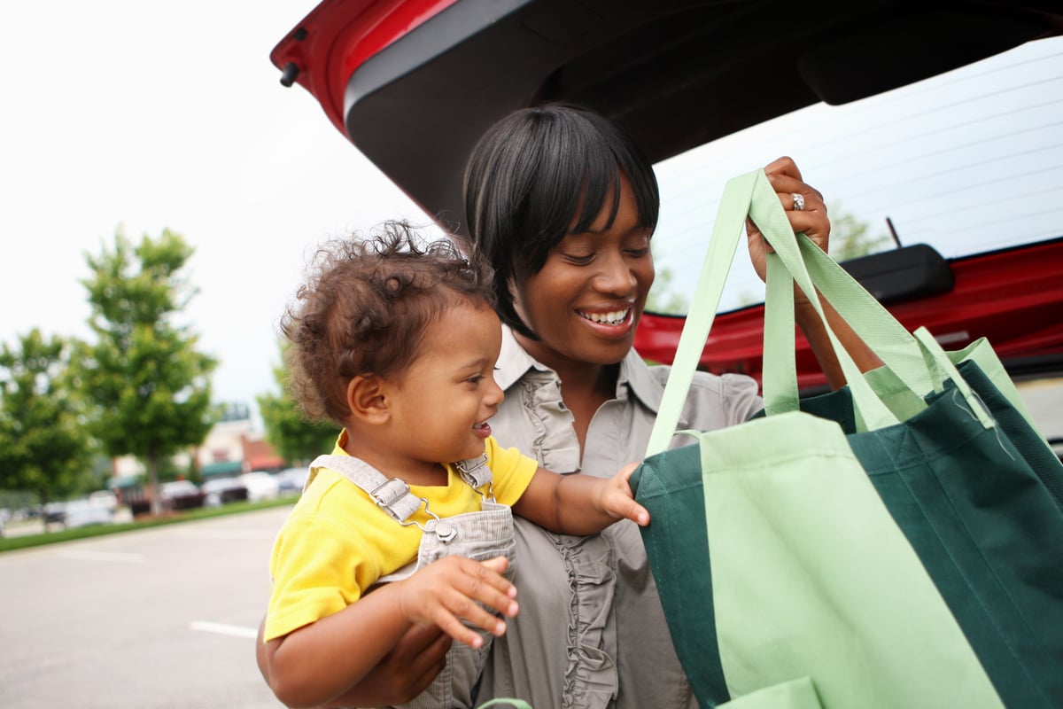 A person with a baby putting grocery bags in a car trunk