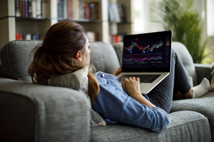 An investor lies on a sofa while trading stocks on a laptop computer.