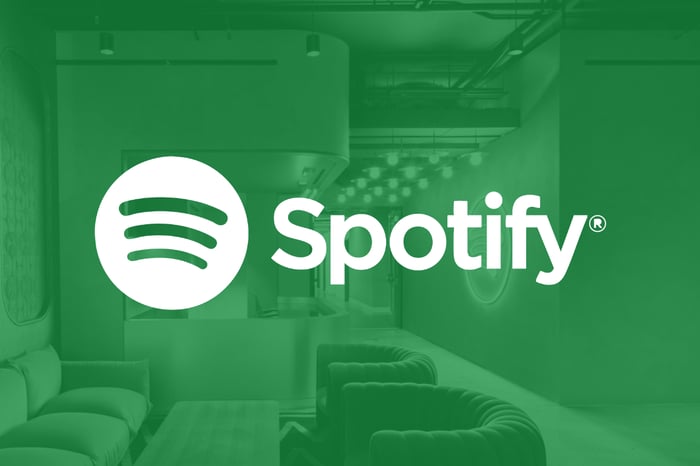 The Spotify logo stands at the forefront against a green backdrop of an office setting.