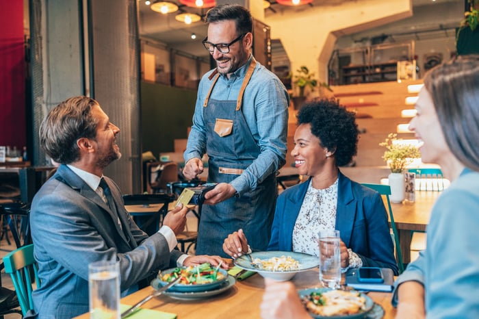 Person making a credit card payment at a restaurant while sitting at a table with two other people.