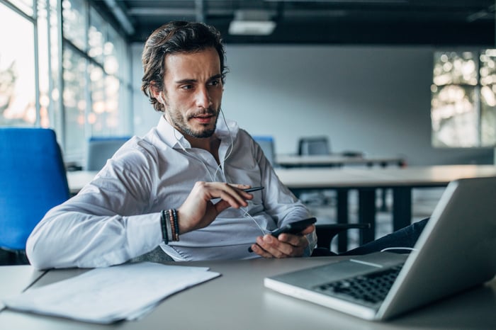 A person is speaking on a mobile phone while looking at a laptop. 