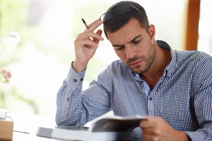An investor looks in consternation at a page in a book while sitting at a desk.
