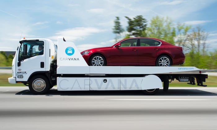 A red sedan being transported on the flatbed of a Carvana delivery truck.