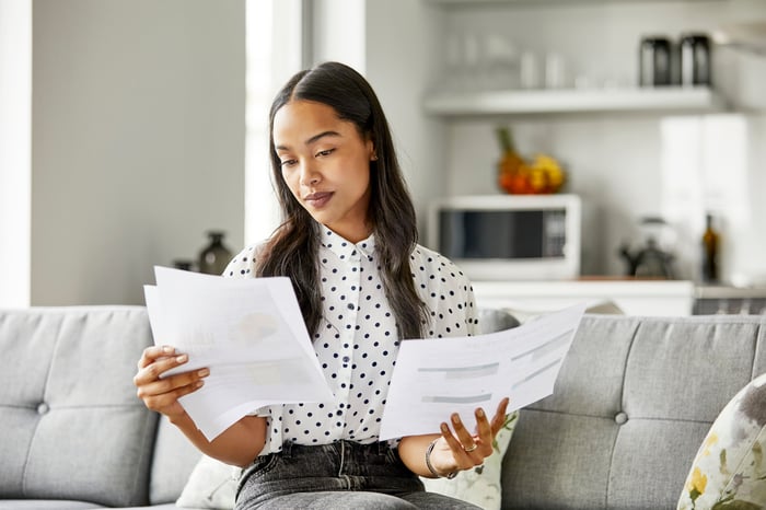 A person sitting on a couch looking at two printouts.