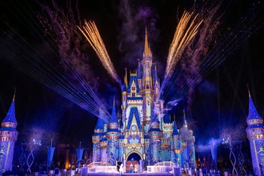 Cinderella Castle at Disney World lit up at night with fireworks exploding overhead
