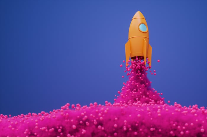 A rocket ship emitting pink spheres, illustrating the stock market’s rise from artificial intelligence (AI) growth stocks.