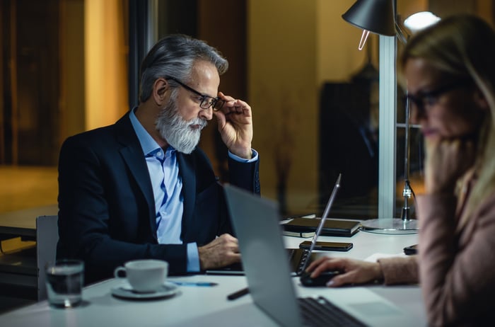 A person wearing eyeglasses is looking at a laptop. 