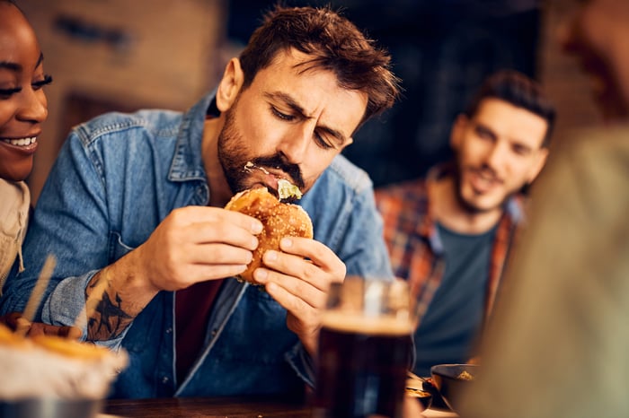 A person at a fast food restaurant biting into a burger. 