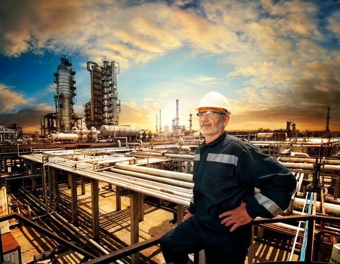 A worker wearing a hard hat near a refinery.