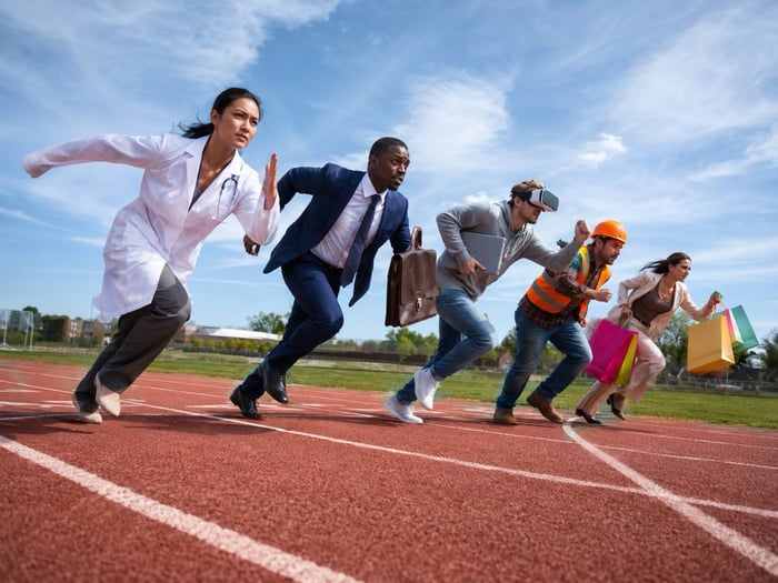 Five people, with a lab coat, a suit and briefcase, a VR headset and laptop, a hard hat, and shopping bags, respectively, run a race on a track.