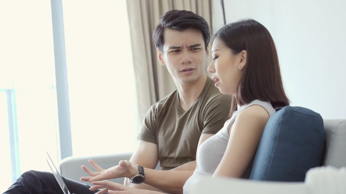 Couple discussing something while one looks at laptop.