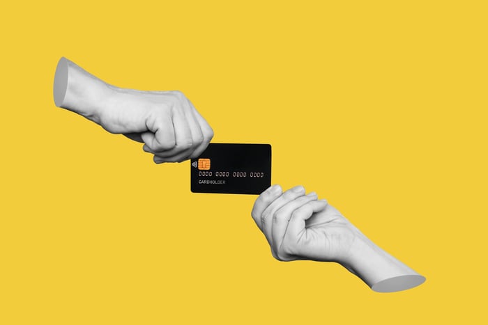 Two hands exchanging a credit or debit card against a yellow background.