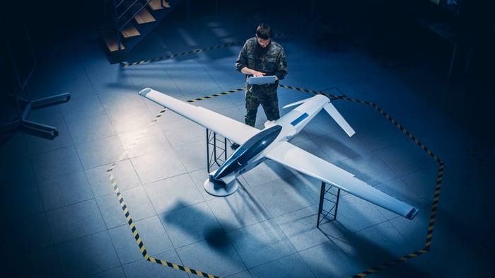 A man working on a laptop as he stand next to a drone.