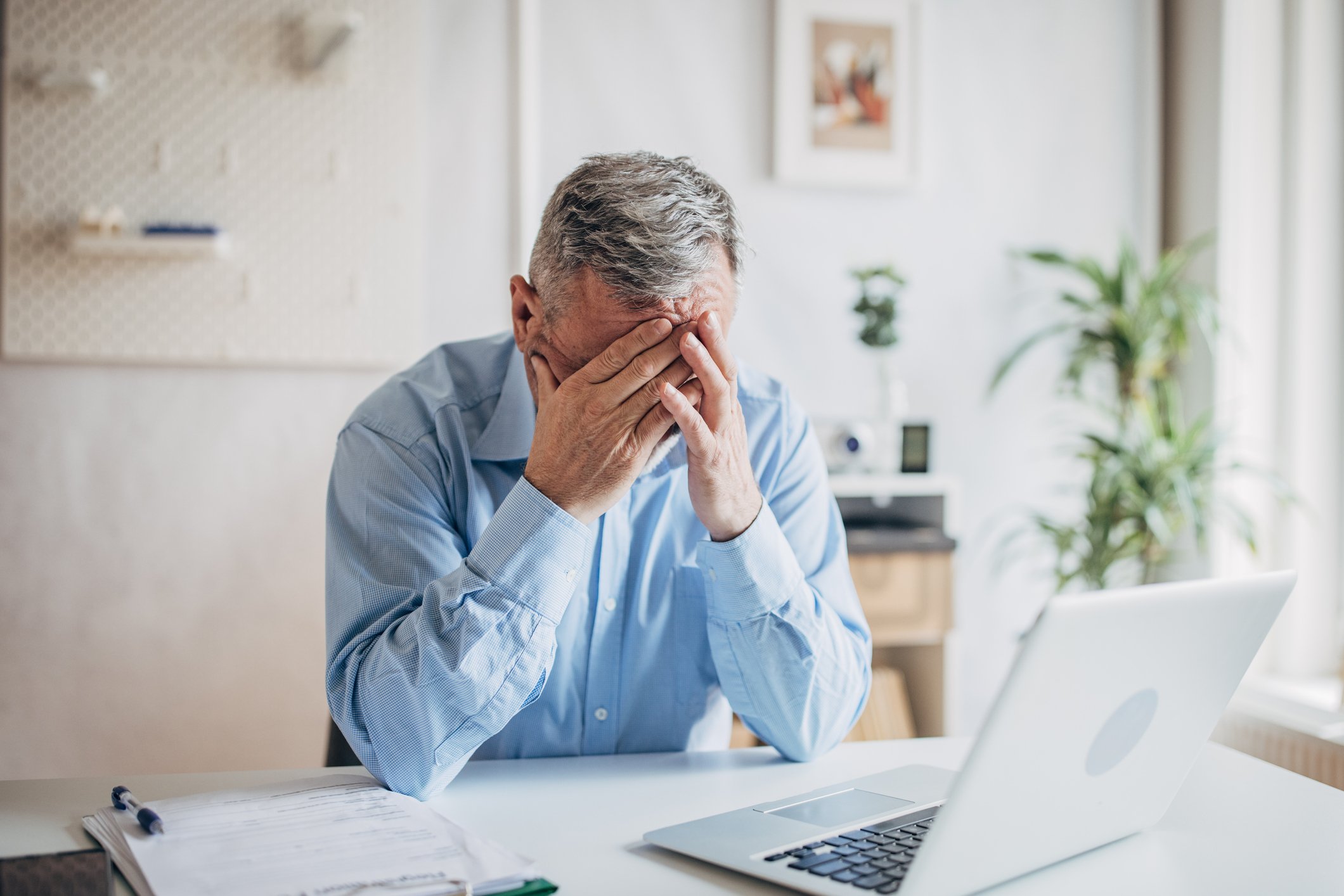 senior man laptop covering face GettyImages-1472263927