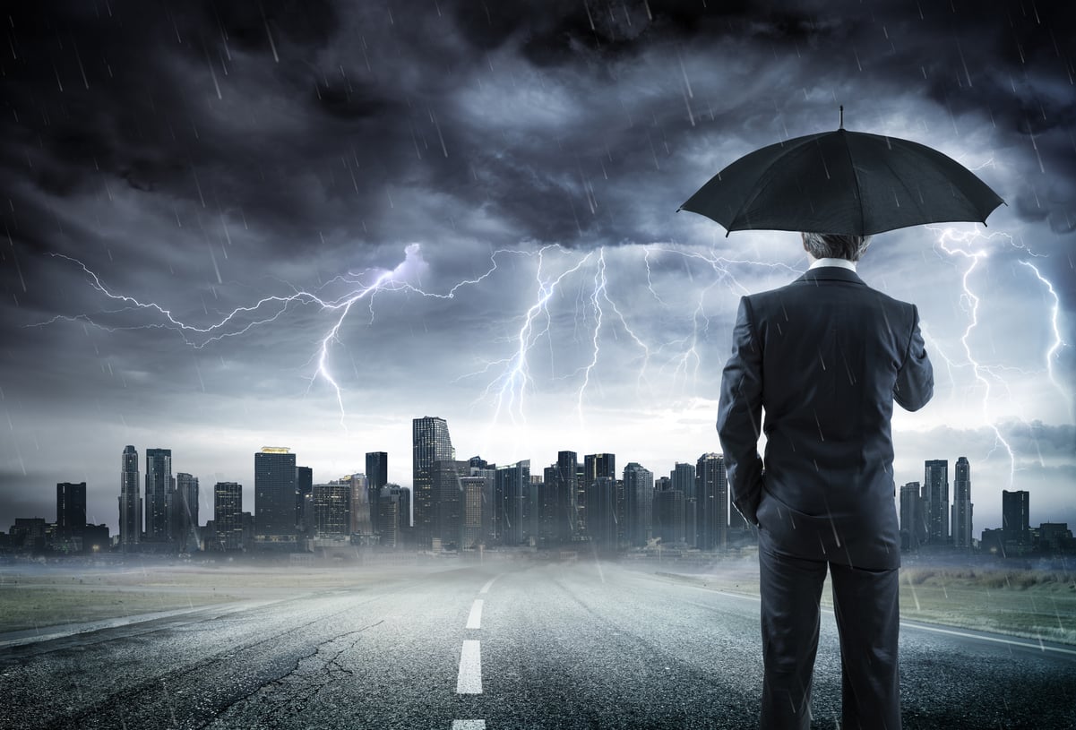 A person wearing a suit and holding an umbrella while standing on a road leading to thunderclouds and lightning crashing down upon a city skyline.