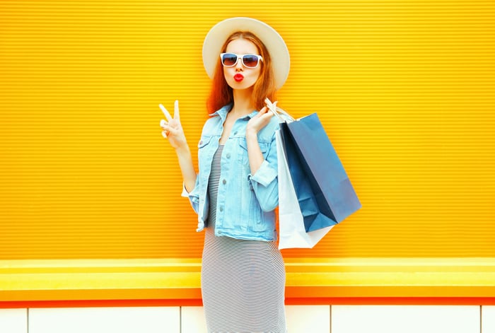 A young woman makes a peace sign while slinging shopping bags over her shoulder.