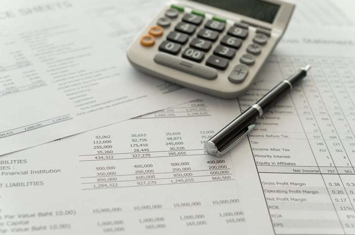 A calculator and pen placed atop several income statements and balance sheets.