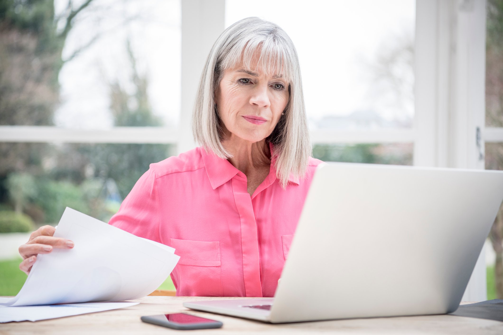 Serious senior holding document and looking at laptop